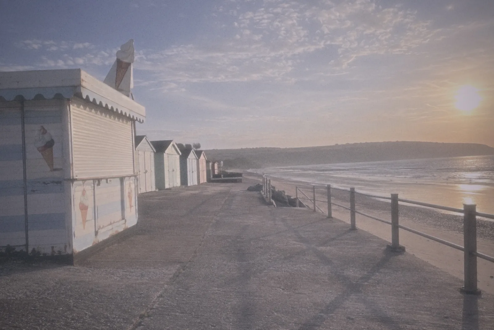 Beach huts and an ice cream kiosk on a seaside promenade at sunset, shot on the ATTIC 85