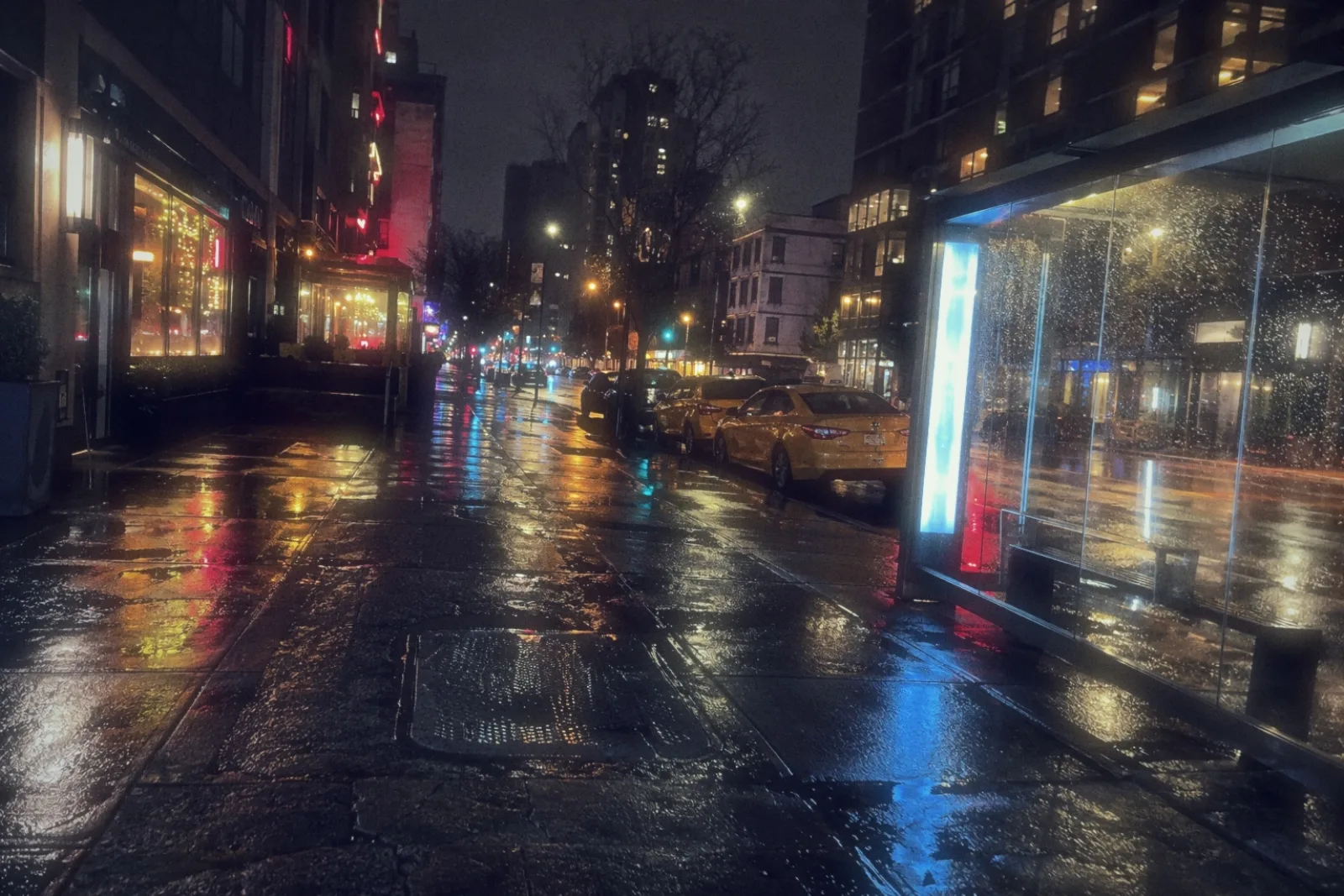 A wet city street at night with taxis and shop lights, shot on the COMPACT 91