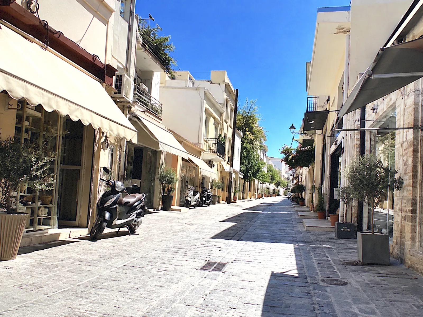 A sunny shopping street with awnings and parked scooters, shot on the DIGI 03